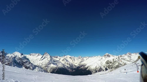 Skier stands on top of the slope against the backdrop of the mountain peaks and prepares to descend. First-person view