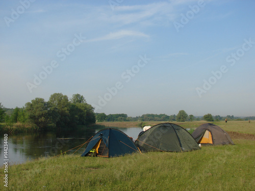 Tent camp on the shore of the flat river on the grass background. Ukraine