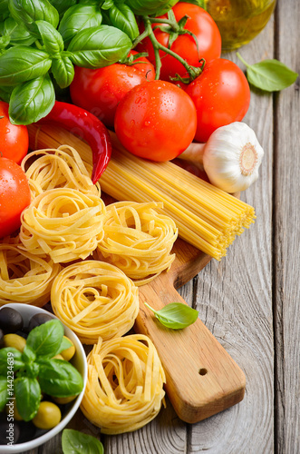 Pasta, vegetables, herbs and spices for Italian food on wooden background, selective focus