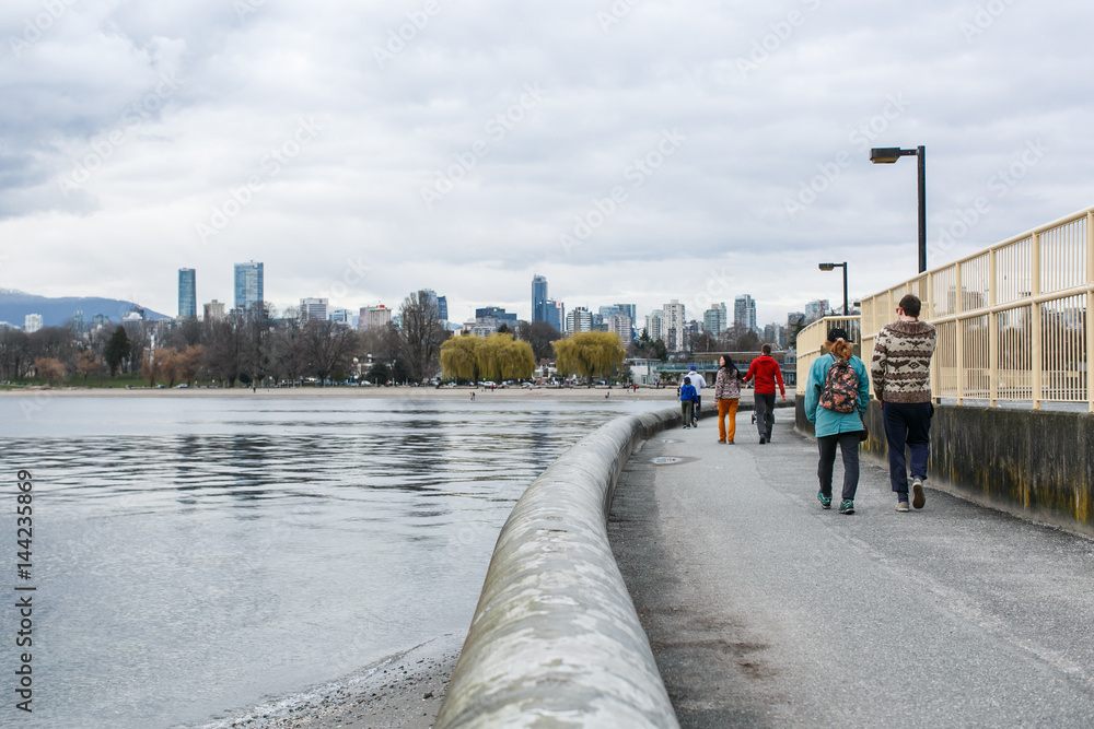 Pedestrians walk along waterfront path in Kitsilano Beach, Vancouver, BC