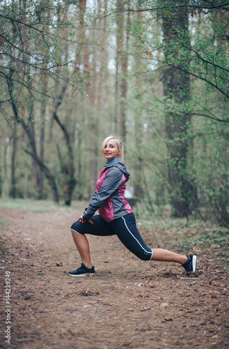 young beautiful girl doing workout in the woods. Blonde girl tracksuit doing exercises