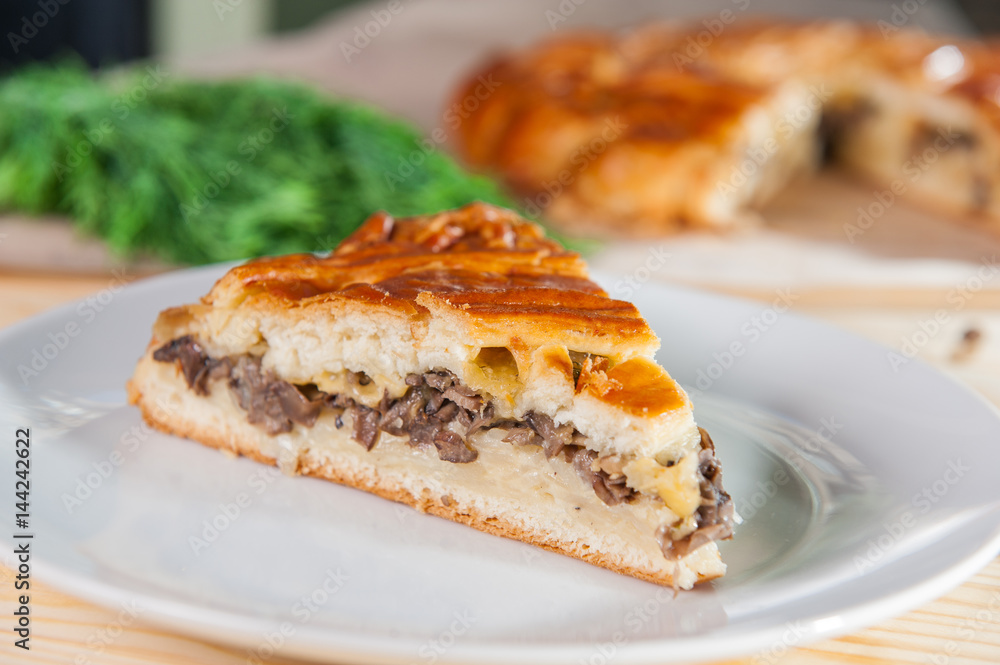 Fresh piece of closed pie with potatoes and mushrooms on the white plate on the wooden served table. Composition of ingridients. Selective Focus, close up Fresh piece of closed pie with potatoes and mushrooms on the white plate on the wooden served table. Composition of ingridients. Selective Focus, close up