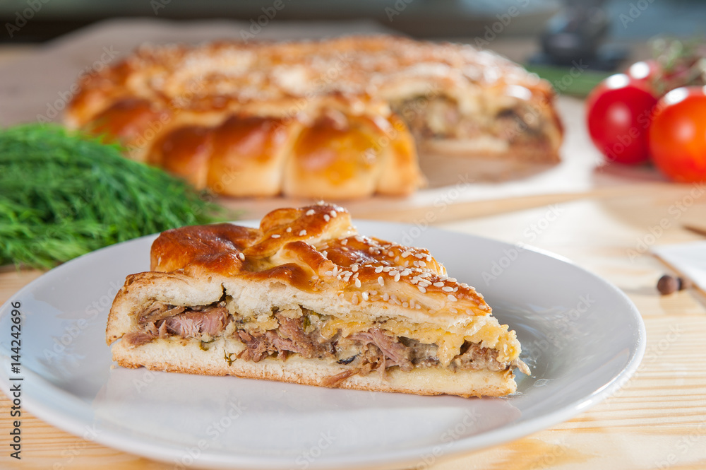 Fresh piece of turkey meat closed pie on the white plate on the wooden served table. Composition of vegetables and ingridients. Selective Focus Fresh piece of turkey meat closed pie on the white plate on the wooden served table. Composition of vegetables and ingridients. Selective Focus