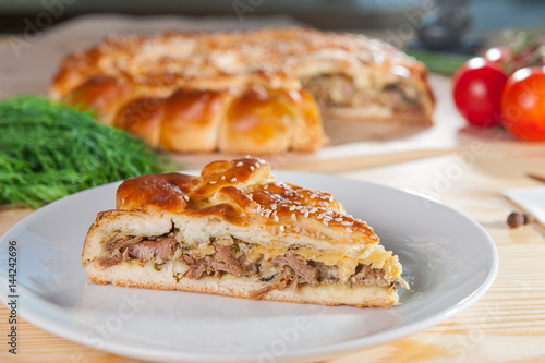 Fresh piece of turkey meat closed pie on the white plate on the wooden served table. Composition of vegetables and ingridients. Selective Focus