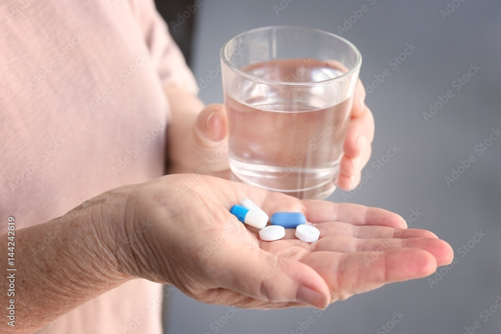 Senior woman with pills and glass of water at home, closeup Senior woman with pills and glass of water at home, closeup