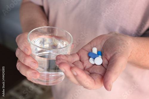 Senior woman with pills and glass of water at home  closeup