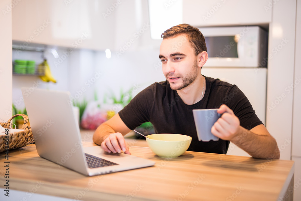 Man eat his breakfast in the kinchen while use laptop in the morning Man eat his breakfast in the kinchen while use laptop in the morning