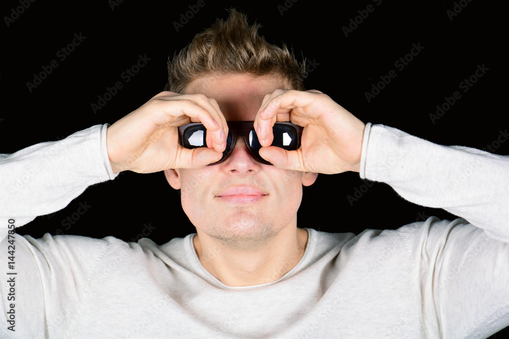 European Young Man in sun glasses looking in binocular isolated on black background