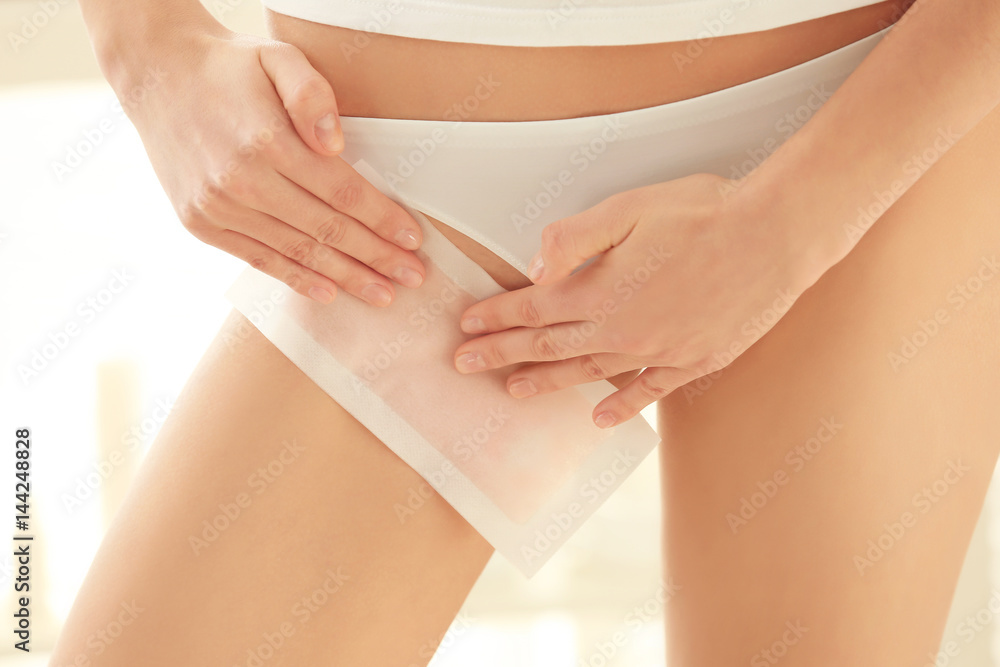 Young woman depilating bikini area with wax on blurred background  Stock-Foto | Adobe Stock