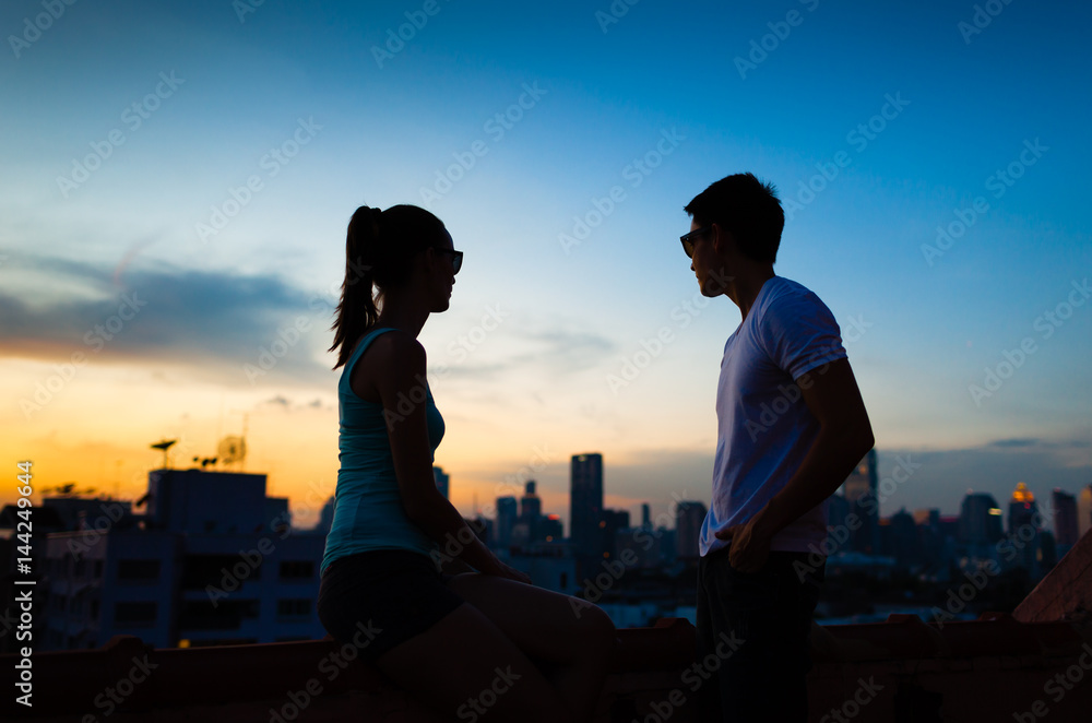 Young man and woman in the city sitting roof top watching the sunset. 