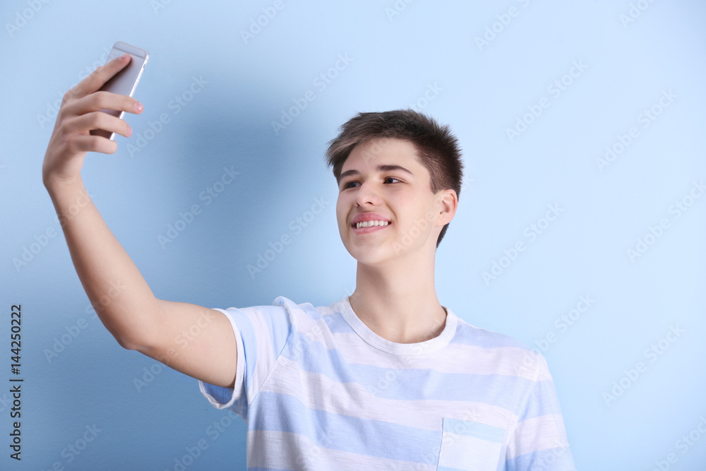 Teenage boy making selfie with mobile phone on light background Teenage boy making selfie with mobile phone on light background