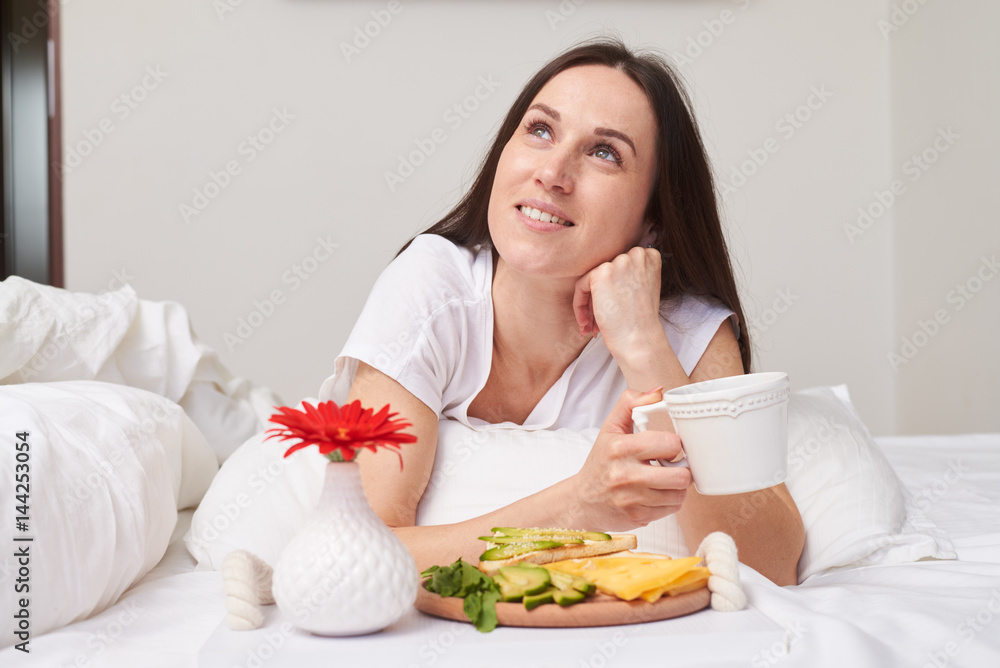 Dreamy smiling brunette enjoying her unforgettable breakfast