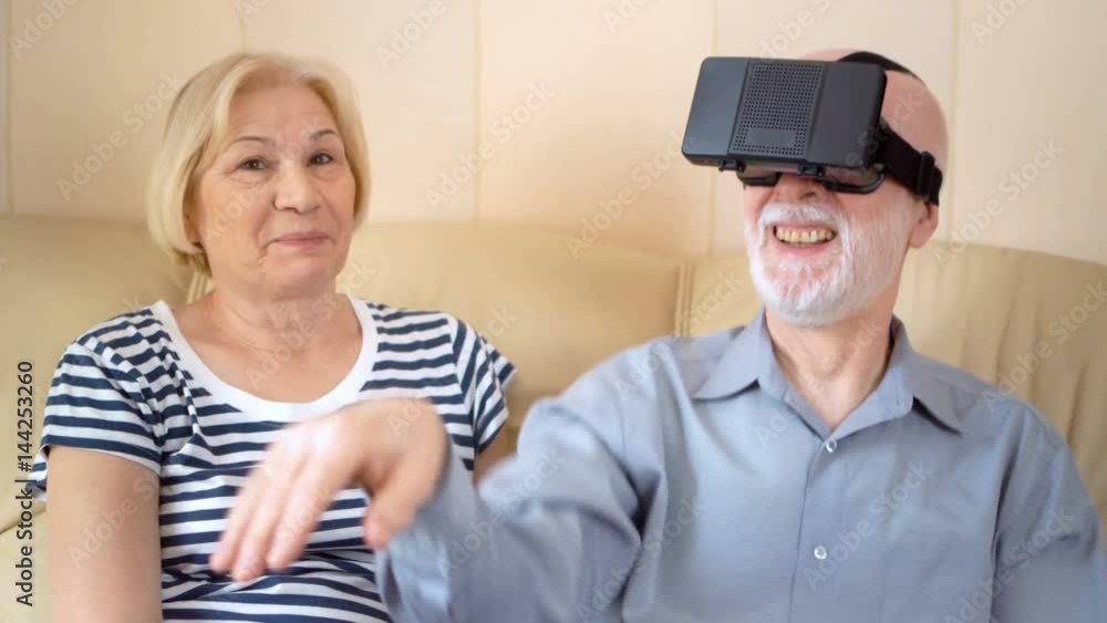 Cheerful good-looking senior couple sitting on sofa at home. Using virtual reality glasses. Cheerful good-looking senior couple sitting on sofa at home. Using virtual reality glasses.