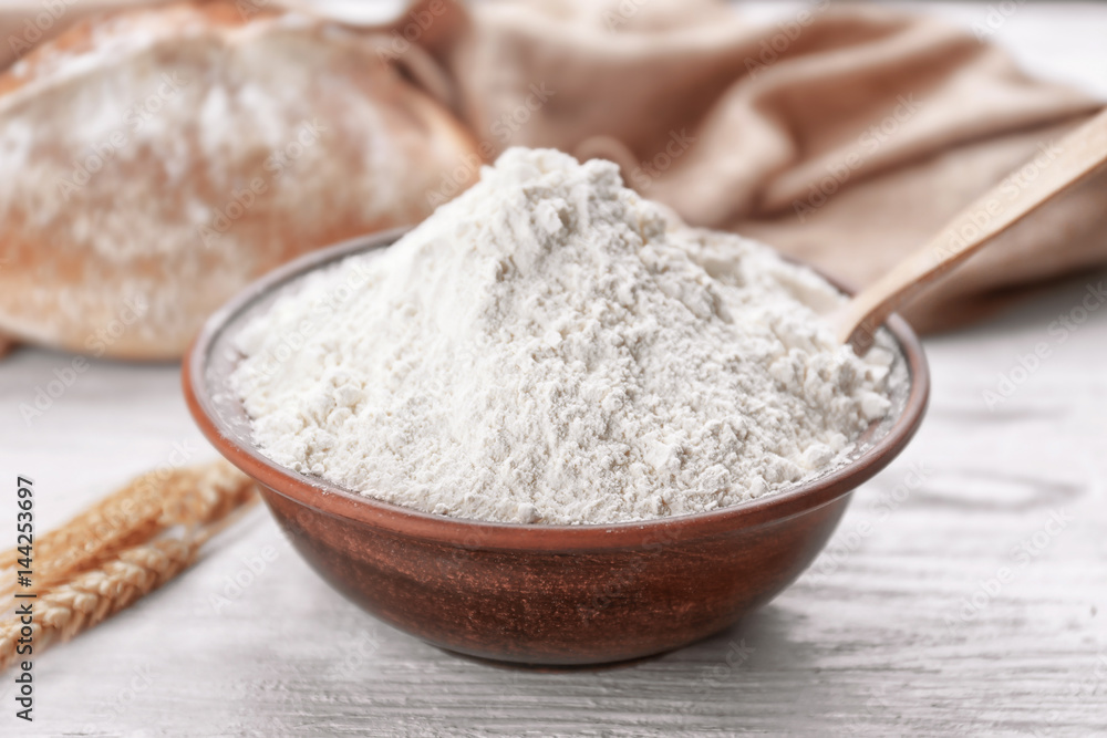 Bowl of white flour, bread and wheat ears on wooden table Bowl of white flour, bread and wheat ears on wooden table