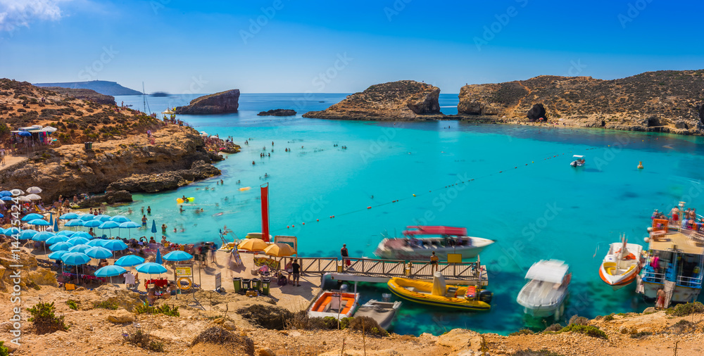 Comino, Malta - Tourists crowd at Blue Lagoon to enjoy the clear turquoise water on a sunny summer day with clear blue sky and boats on Comino island, Malta. - obrazy, fototapety, plakaty 