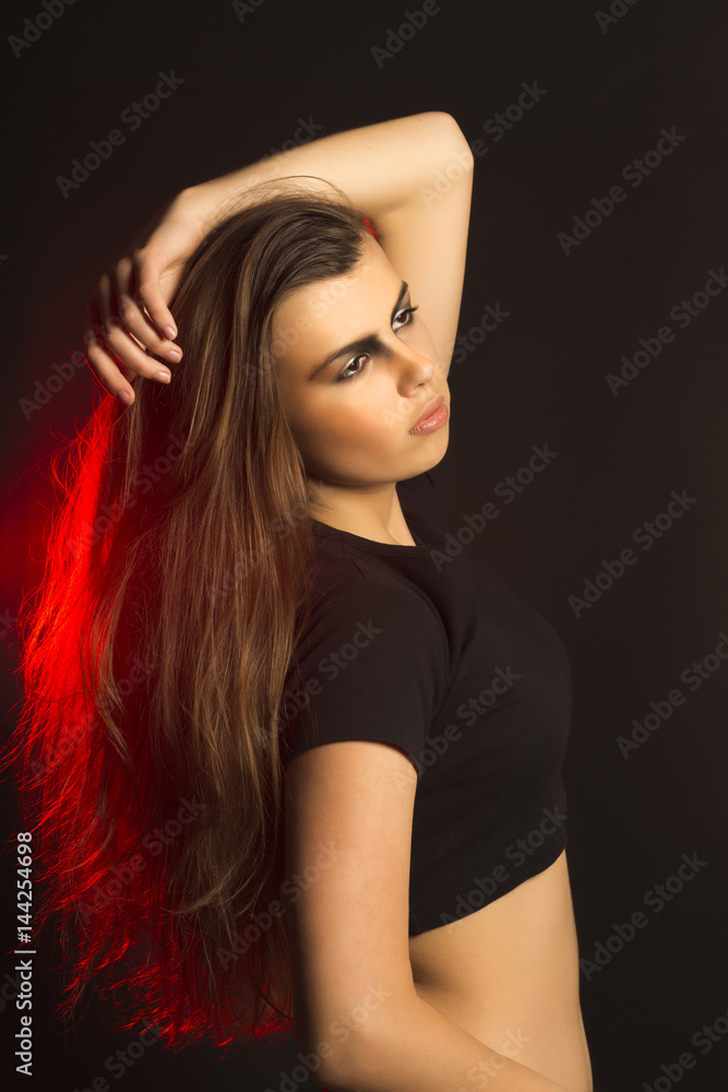 Naklejka premium Fashionable brunette woman with art makeup at studio with red light