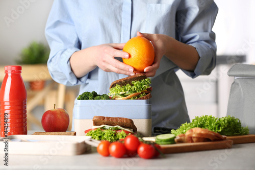 Mother packing meal for school lunch on table