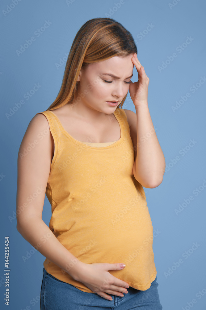 Pregnant woman suffering from headaches on blue background Pregnant woman suffering from headaches on blue background