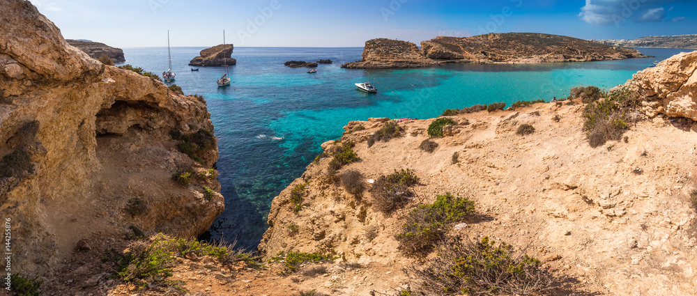 Comino, Malta - The beautiful Blue Lagoon with turquoise clear sea water, yachts and snorkeling tourists on a sunny summer day with the island of Gozo at background