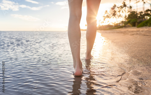 Woman's feet walking along a beautiful beach in Hawaii at sunset. 