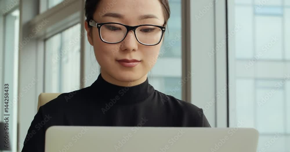 closeup of a young successful Asian business girl in a modern office, working using laptop closeup of a young successful Asian business girl in a modern office, working using laptop