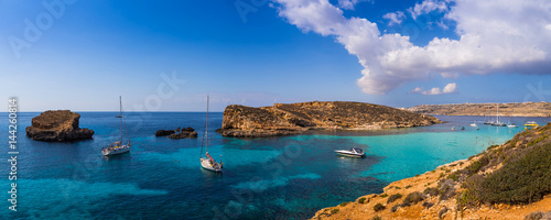 Comino, Malta - Panoramic skyline view of the beautiful Blue Lagoon on the island of Comino with sailboats, traditional Luzzu boats and tourists enjoying the mediterranean sea