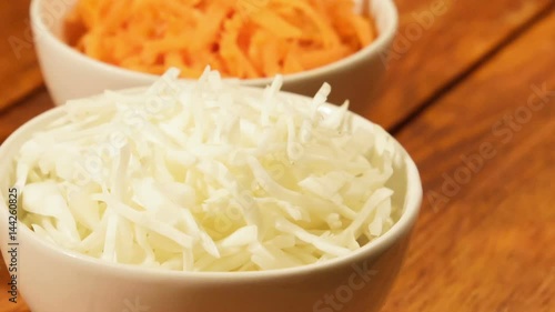 Chopped carrot and cabbage in white cup on wooden background close up. Ingredients for vegetable salad
