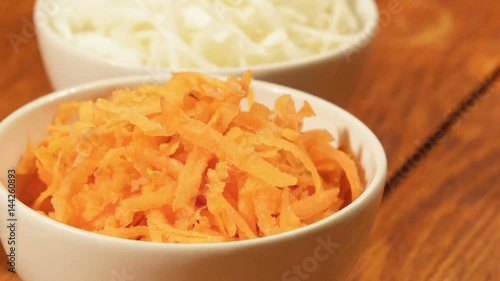Chopped carrot and cabbage in white cup on wooden background close up. Ingredients for vegetable salad