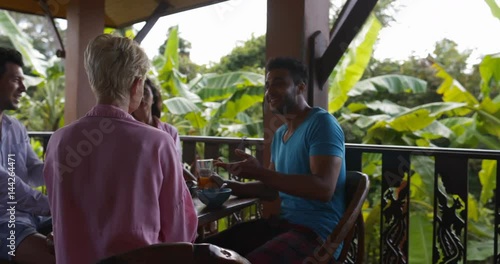 Terrace In Tropical Forest, People Having Breakfast Clonking Juice Glassses Sit At Table Talking, Man And Woman Group Morning Slow Motion 60 photo