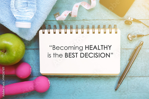 Fitness motivation quotes written on open notebook. Fitness equipment on wooden background.