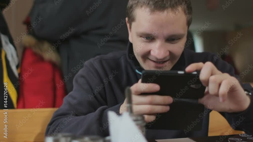 Young man using smartphone, smiling and talking with someone. Cafe interior Young man using smartphone, smiling and talking with someone. Cafe interior