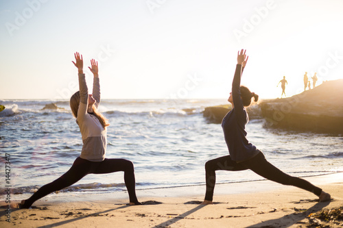 Two girls on the beach doing yoga at sunset time. California. San Diego. Woman doing yoga pose. Hand up