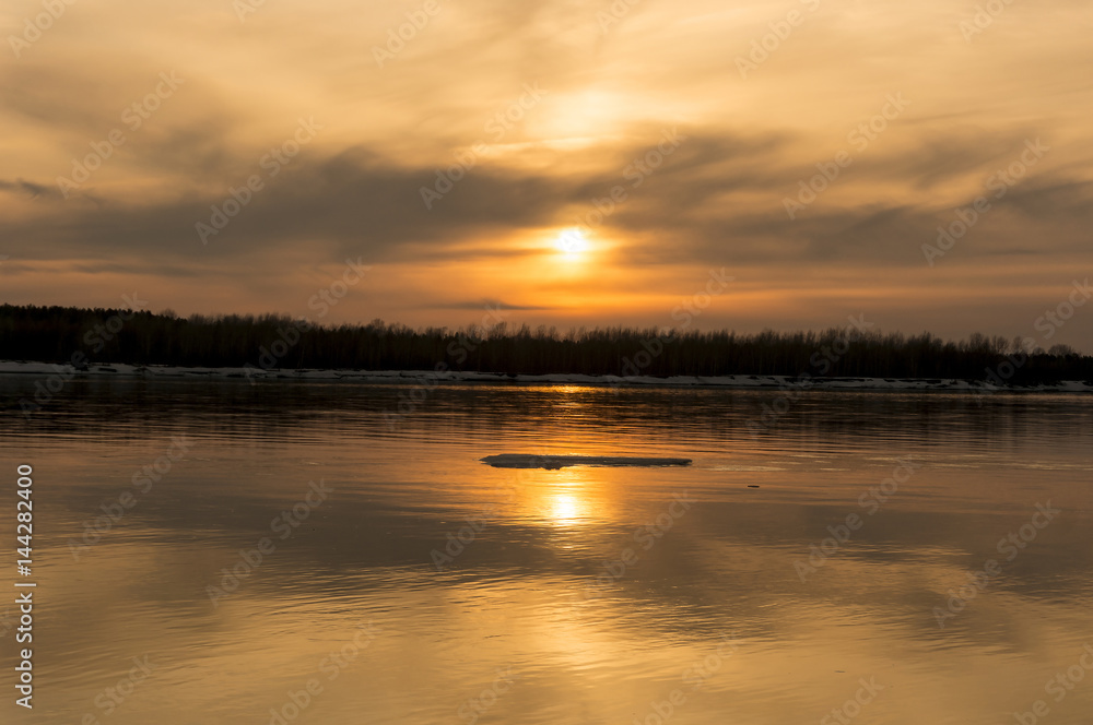 Obraz premium Orange sunset on the river bank. Reflection of the sunset in the water. The ice floes on the water.