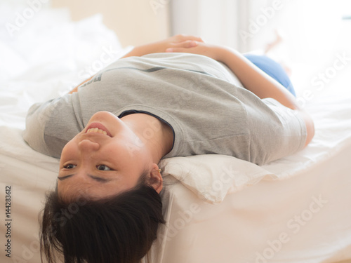 smiling young chinese woman lying upside down on the bed