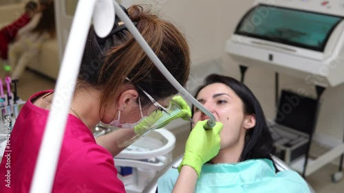 Dentist cleans woman's teeth with professional toothpaste and automatic brush. Dentist using saliva ejector or dental pump to evacuate saliva. photo