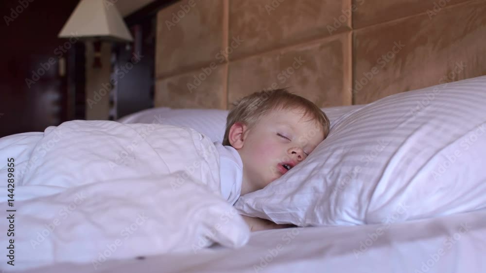 The little boy is sleeping in the bed, mother caresses him gently on the head. The little boy is sleeping in the bed, mother caresses him gently on the head.