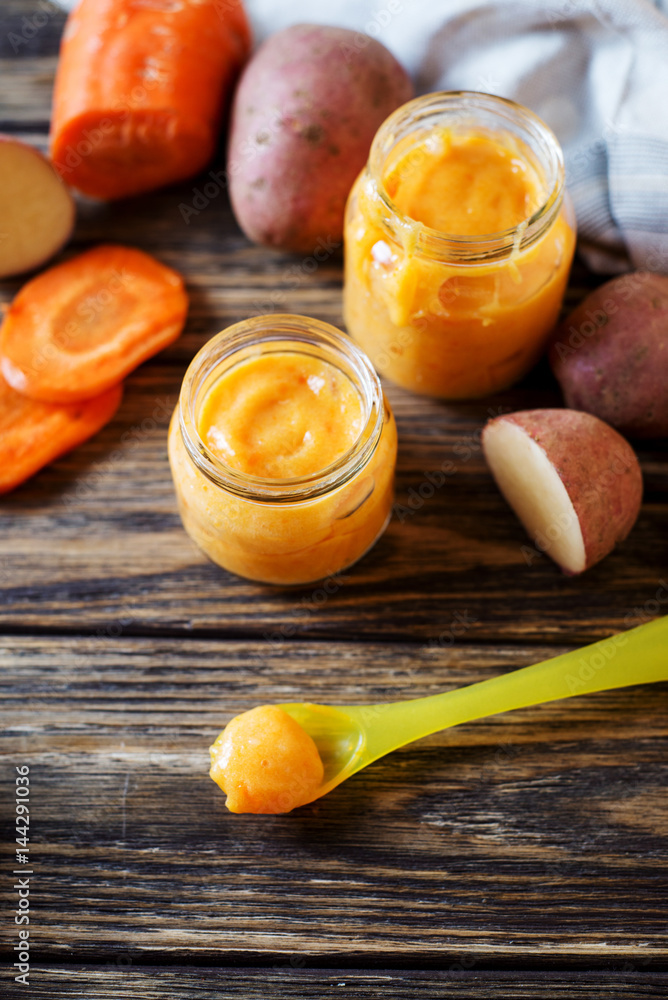 Food for kids, children's lure, organic puree from boiled potatoes and carrot in small glass jars on a dark rustic wooden background Food for kids, children's lure, organic puree from boiled potatoes and carrot in small glass jars on a dark rustic wooden background
