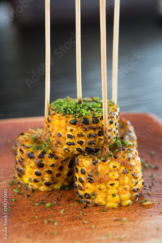 Grilled spicy sweetcorn on the cob, lightly covered with spices and chives, served on a wooden board and skewer. photo