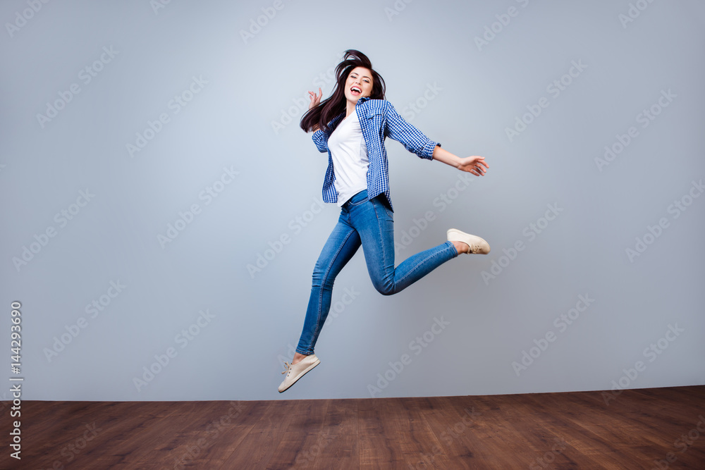 Young beautiful woman in checkered shirt jumping up against gray background