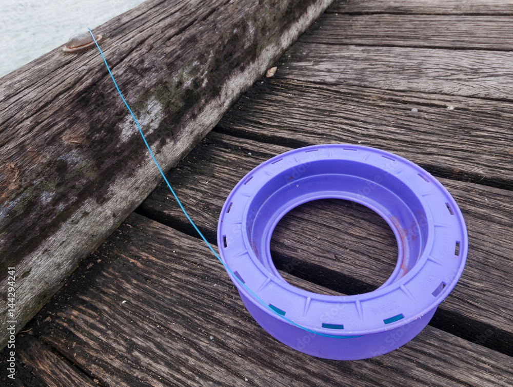 A purple plastic handline and blue fishing line, setup on a wooden