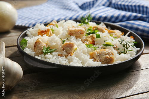 Delicious rice with chicken in pan on wooden table
