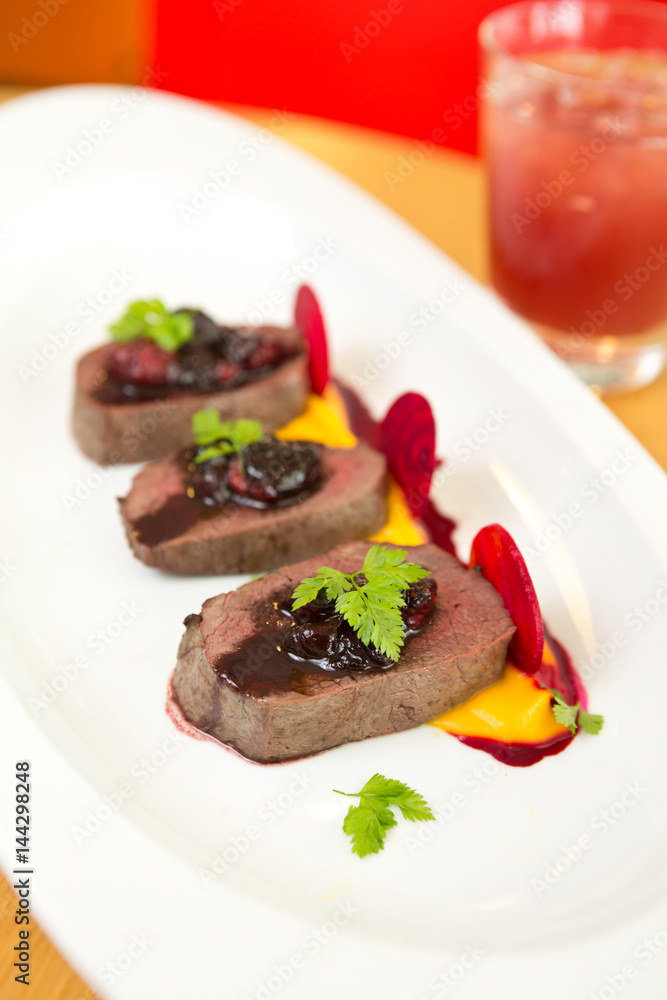 Organic Venison served with fresh raspberry raspberry sauce, beetroot slices and pumpkin puree, on a white plate.