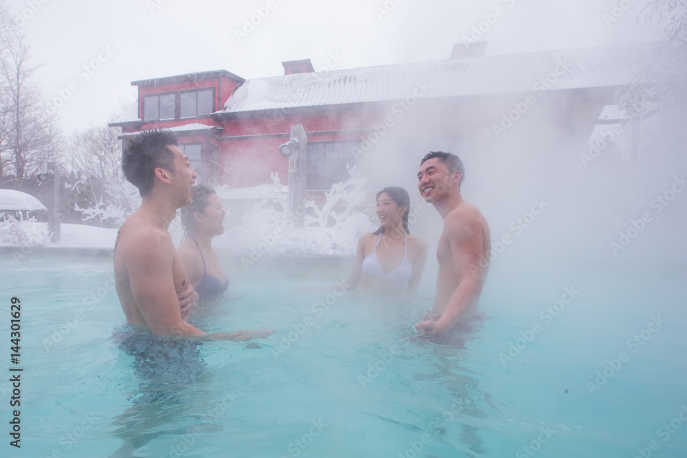 Ethnic couples relax in outdoor spa during winter