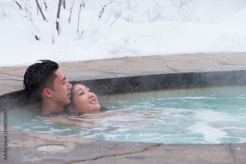 Ethnic couple relaxes in outdoor spa during winter