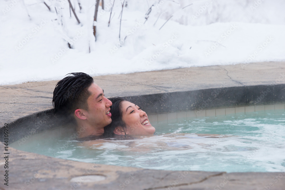 Ethnic couple relaxes in outdoor spa during winter