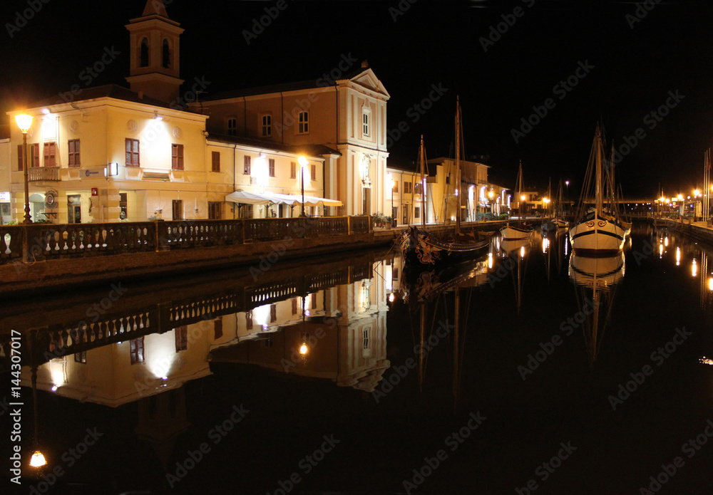 Italy. Emilia-romagna. Cesenatico. Canal of night town on black sky background, horizontal view.