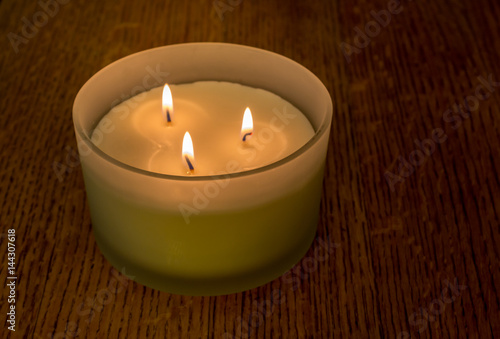 Three flame scented candle in matte glass holder on oak wood table close up