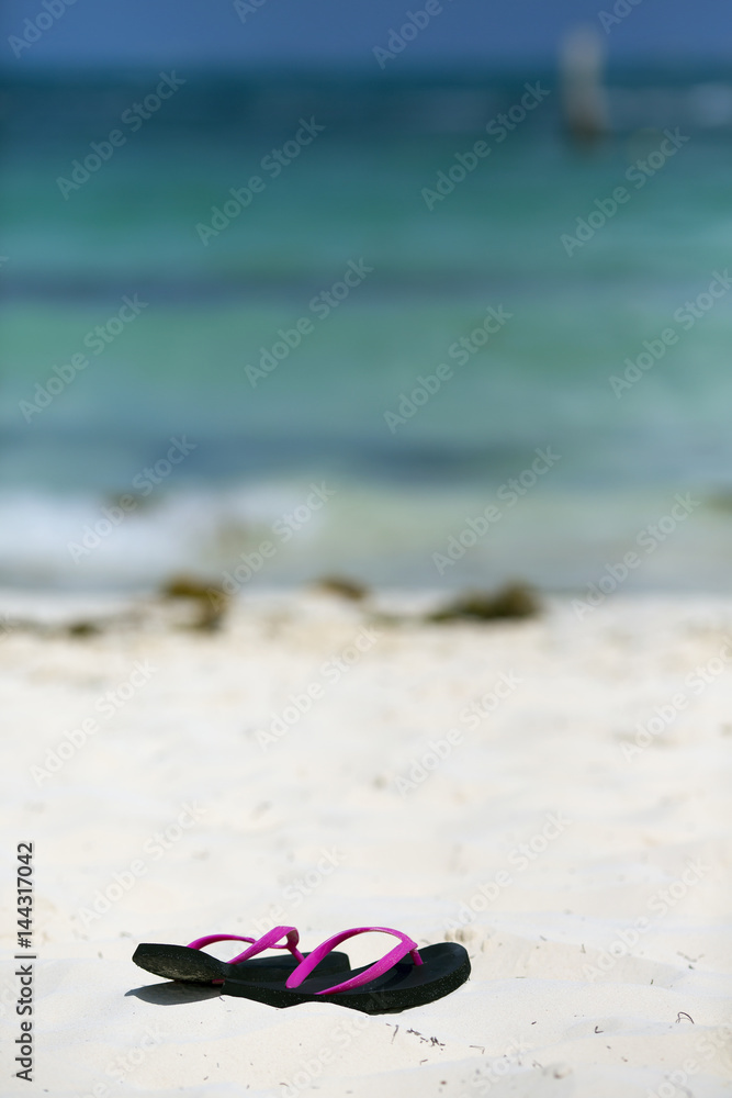 Naklejka premium Sandals on the beach. White sand. Turquoise water. Focus point on the flip-flops.