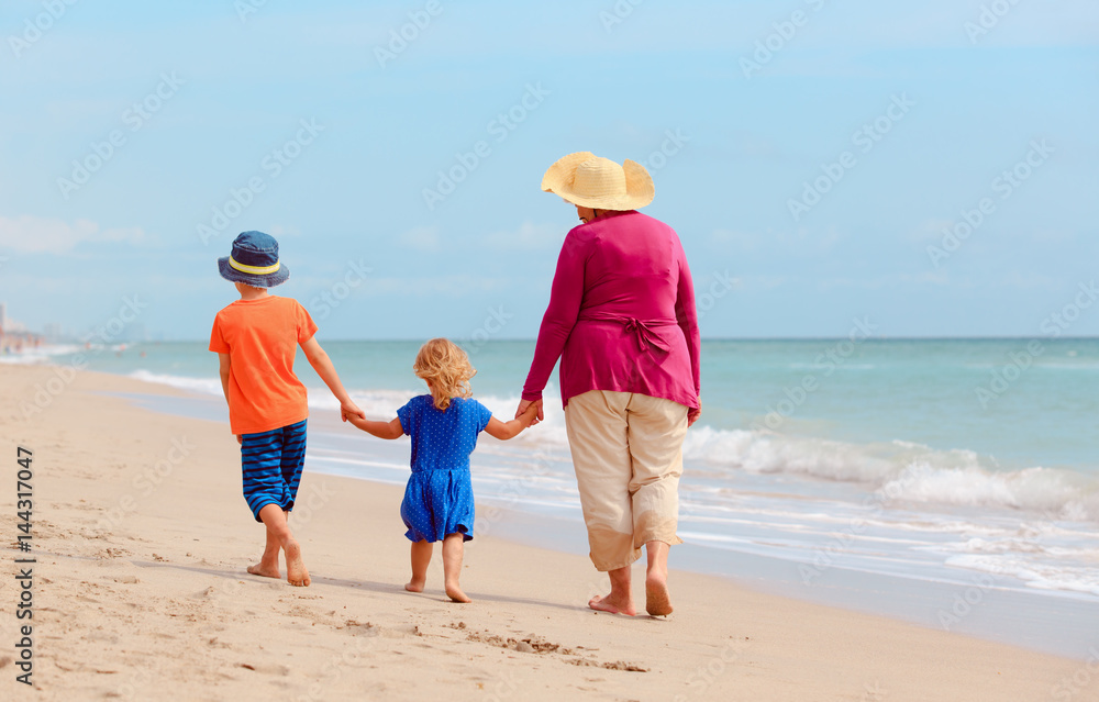 grandmother with grandkids- little boy and girl- walk at beach