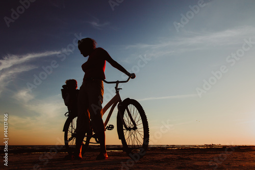 Silhouette of mother and baby biking at sunset